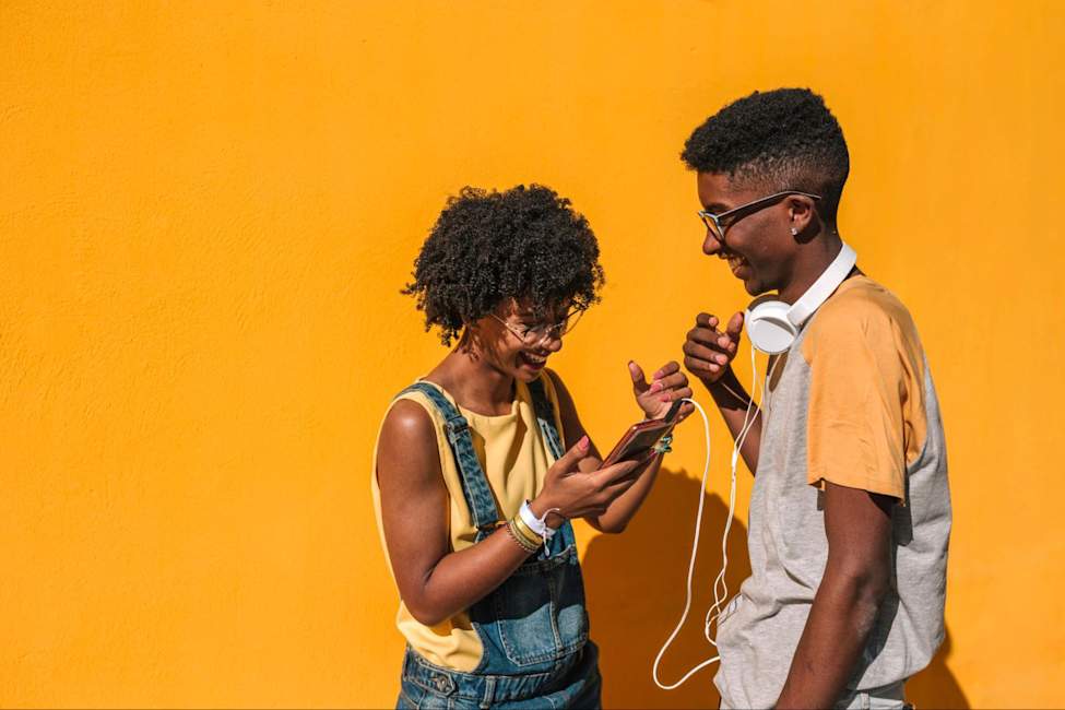 Two friends laughing together while looking at a phone, representing authentic social connection.