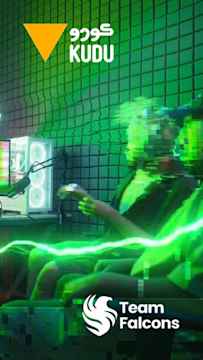 Une personne filmant en streaming dans une pièce éclairée en vert avec l'inscription « KUDU » en anglais et en arabe, un triangle orange et le logo de « Team Falcons ».