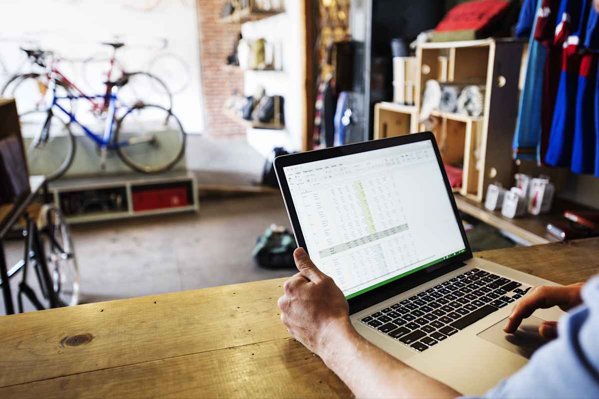 Man in a bicycle shop interacting with a spreadsheet on his laptop